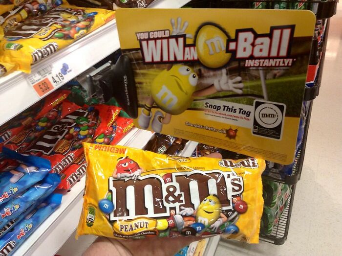 Bag of peanut M&M’s on a grocery store shelf with promotional sign.
