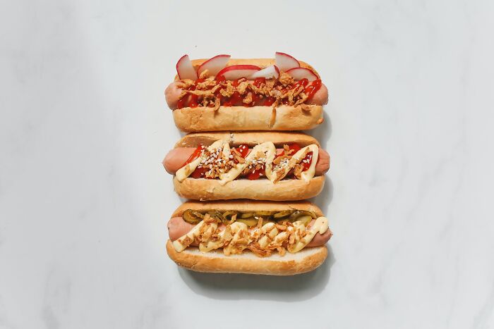Three gourmet hot dogs with various toppings on a white background, highlighting popular grocery store items.