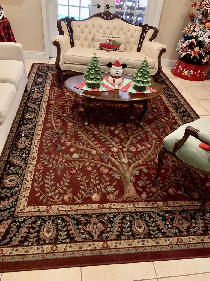 Vintage ornate rug with a tree design in a living room, surrounded by antique furniture and holiday decor from thrift stores.