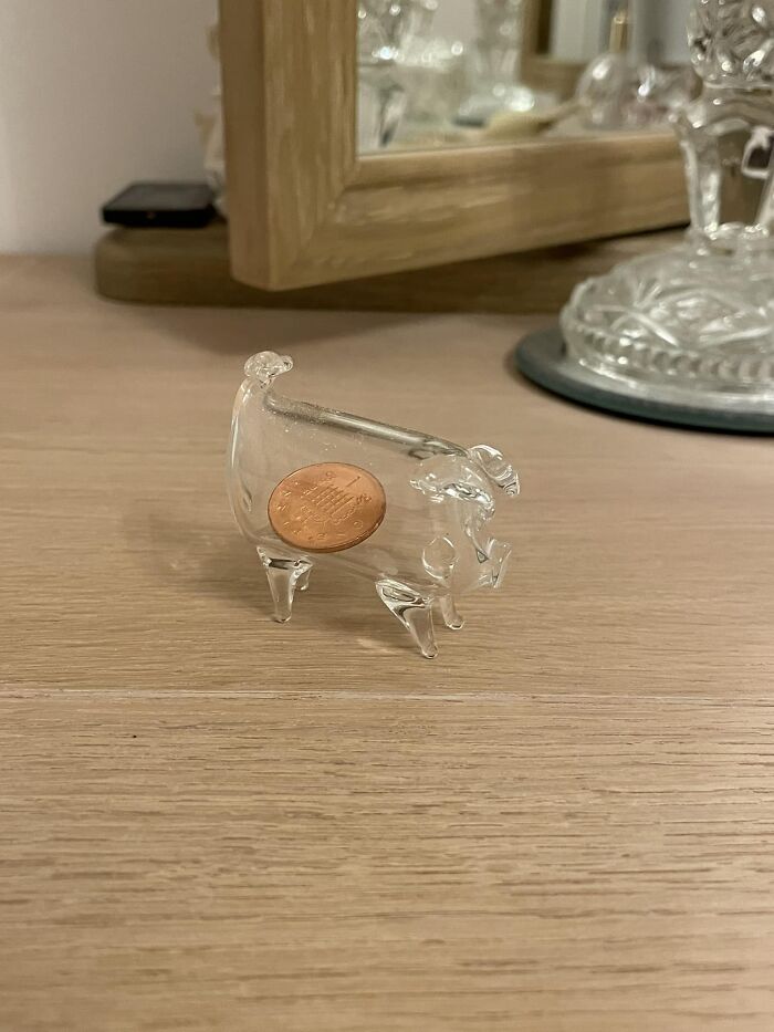 Clear glass pig figurine found at a thrift store with a penny inside it, sitting on a wooden surface near a mirror.