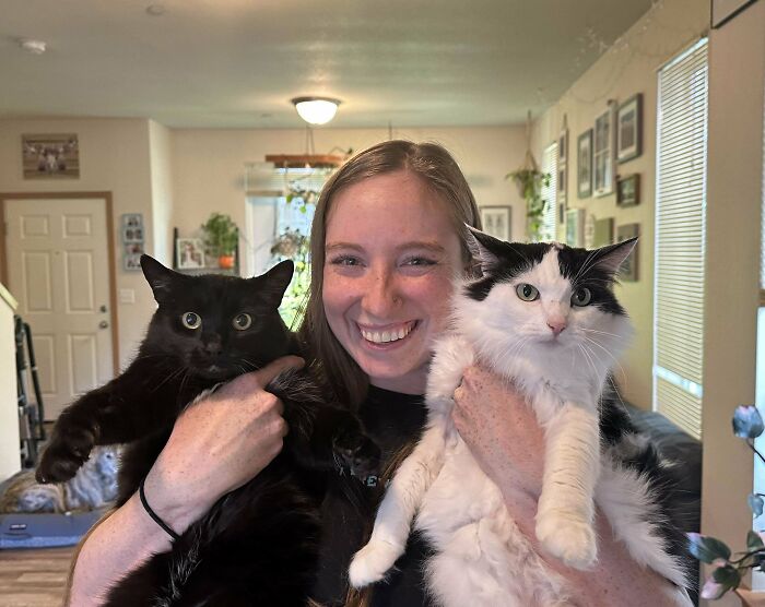 Woman smiling while holding two fluffy cats indoors, showcasing some of the cutest cats sure to melt your heart