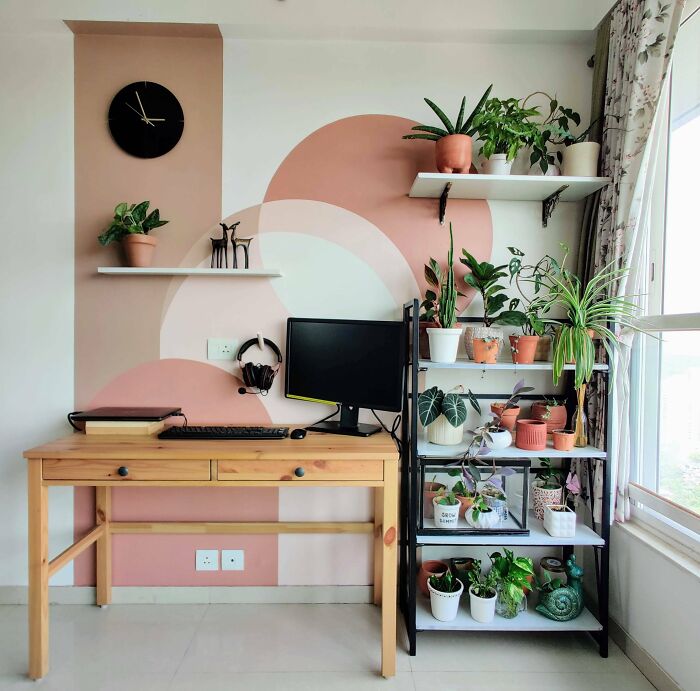 Home decoration with plants on shelves and a desk in a stylish workspace with a pink geometric accent wall.