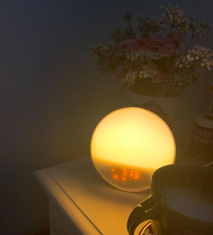 Sunrise alarm clock on a bedside table beside flowers and a mug, ideal for simplifying your daily routine.