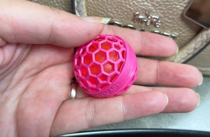Hand holding a small pink and red plastic mesh ball demonstrating one of the useful life hacks from this year's rollercoaster.