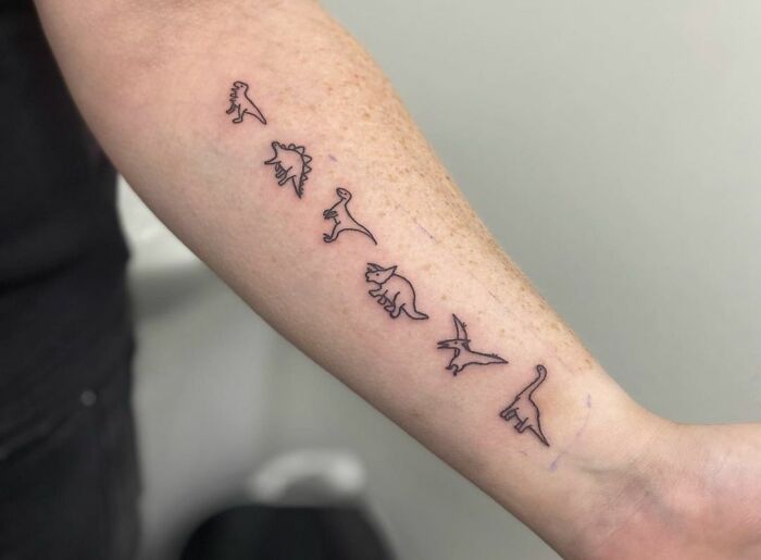 Minimalist dinosaur tattoos on forearm, showcasing small, detailed designs.