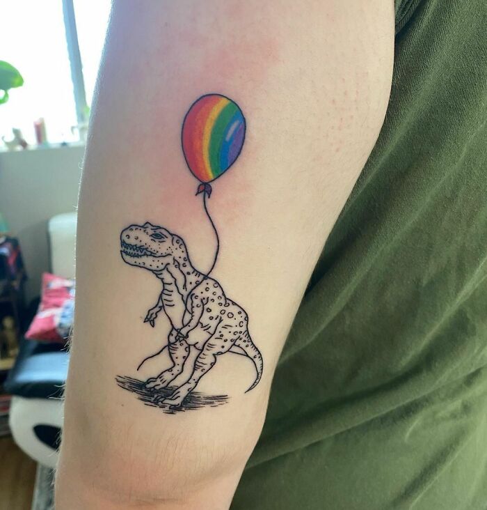 Dinosaur tattoo of a T-Rex holding a rainbow balloon, perfectly executed on the arm.