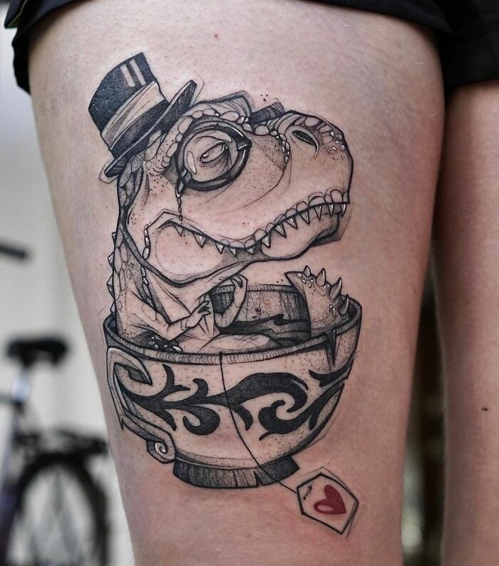 Cool dinosaur tattoo of a T. rex wearing a top hat and glasses, sitting in a teacup with a heart-shaped tag.