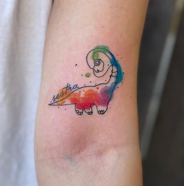 Colorful dinosaur tattoo on arm, featuring abstract watercolor style and creative design.