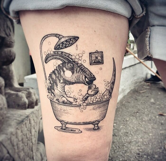 Creative dinosaur tattoo of a Parasaurolophus in a bathtub with bubbles on a person's thigh.
