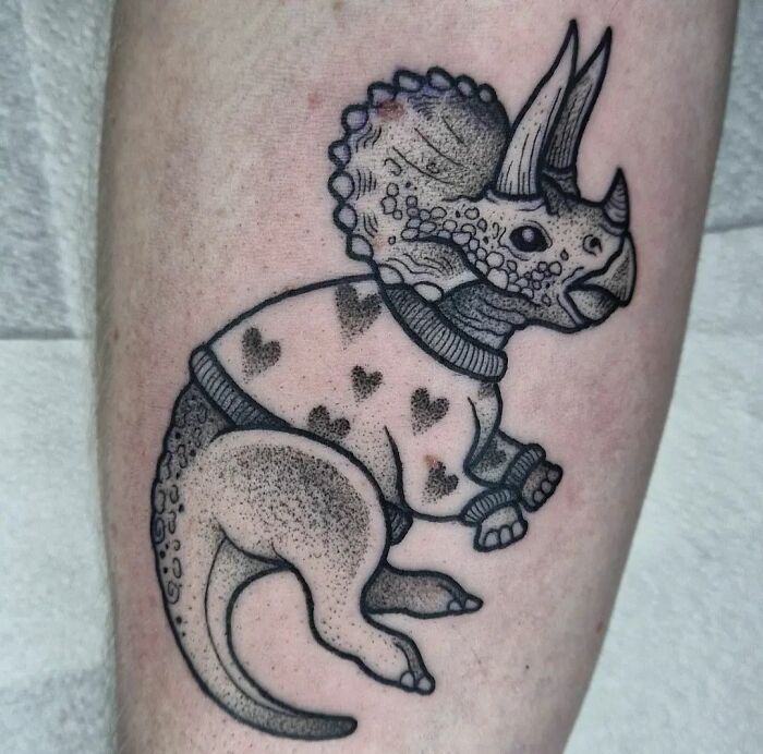 Cool dinosaur tattoo on forearm featuring a Triceratops in a cozy sweater, showcasing creative tattoo art.