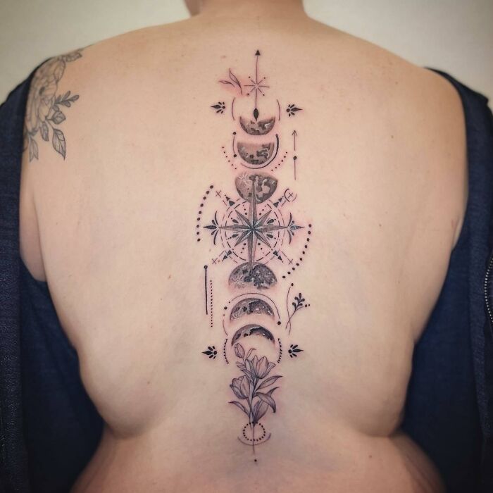 Spine tattoo featuring moon phases, compass, and floral design on a person's back.