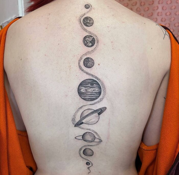 Spine tattoo featuring solar system planets in black ink on a person's back, highlighting beautiful design elements.