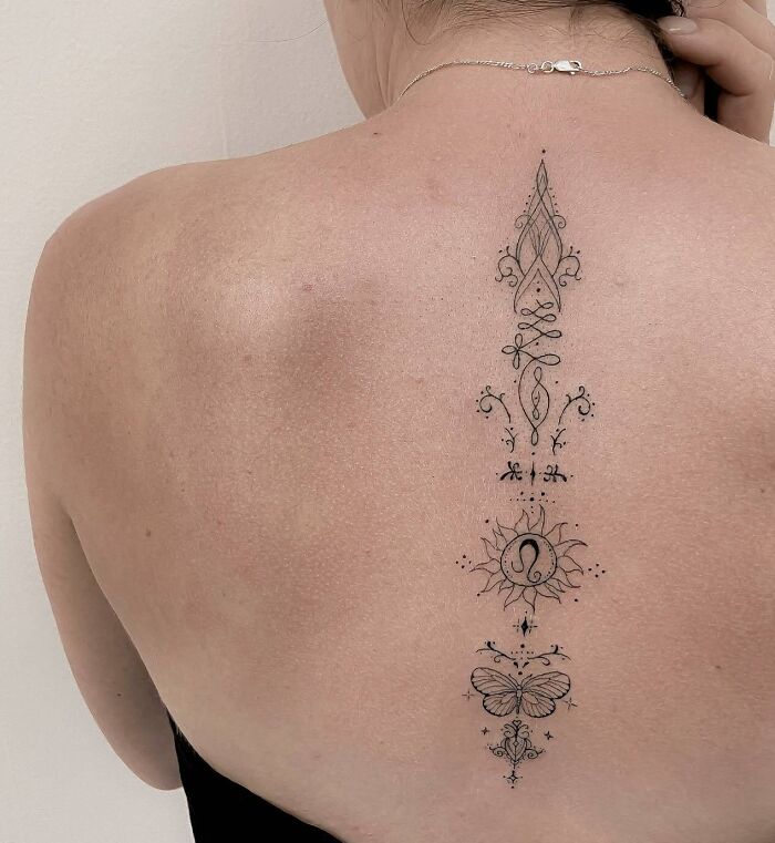 Intricate spine tattoo featuring delicate designs, including a sun and butterfly, on a person's back.