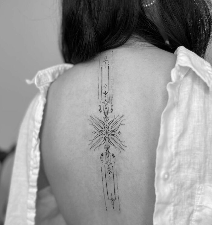 Intricate spine tattoo design on a person's back, showcasing detailed linework and symmetry.