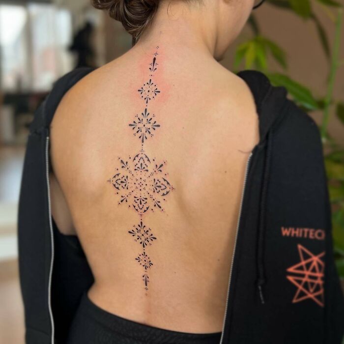 Intricate spine tattoo with geometric patterns on a person's back.