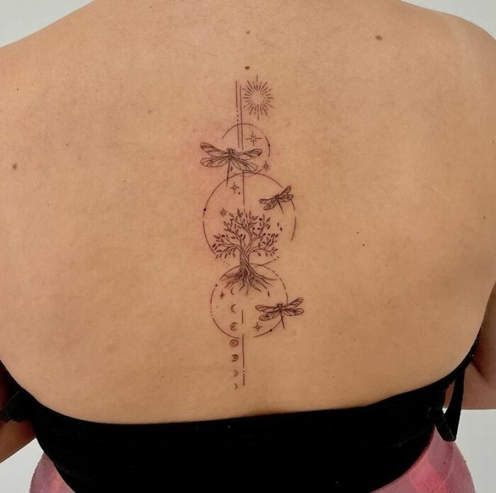 Elegant spine tattoo of tree, dragonflies, and celestial symbols on back.