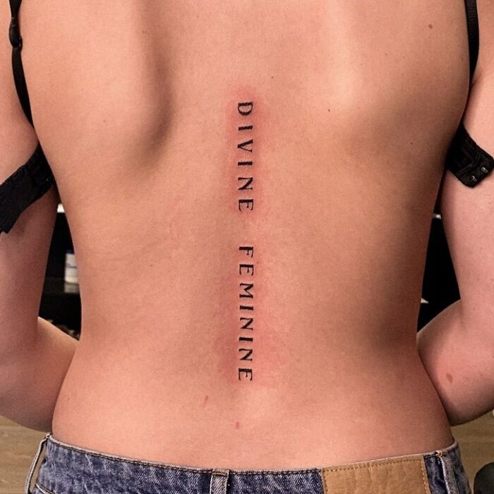 Beautiful spine tattoo reading "Divine Feminine" vertically along the back.