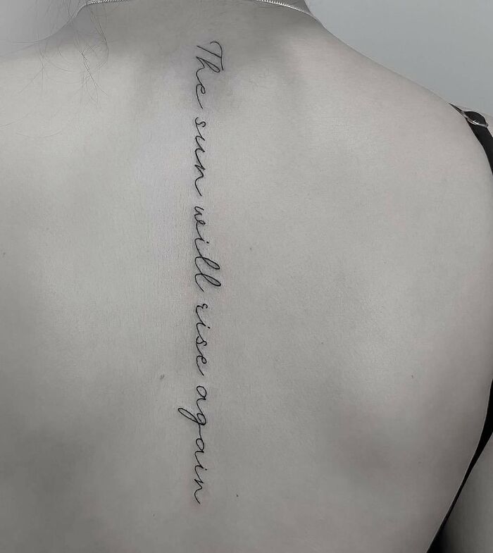 Elegant script spine tattoo with the phrase "The sun will rise again."