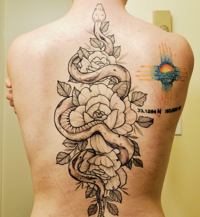 An intricate spine tattoo featuring a snake entwined with flowers and a colorful sun design on the back.