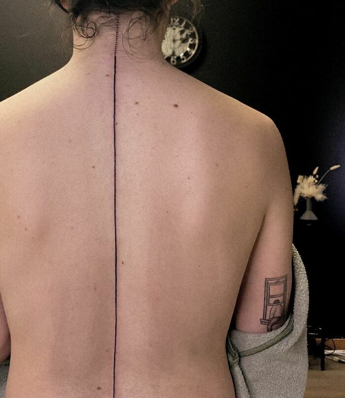 Bare back featuring a linear spine tattoo in a minimalist room.