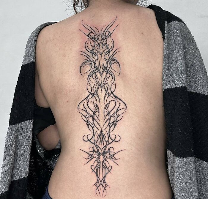 Intricate spine tattoo design on a woman's back, showcasing elegant, symmetrical patterns.