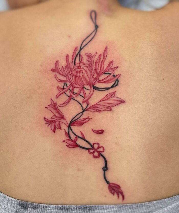 Floral spine tattoo in red and black ink with intricate design on skin.
