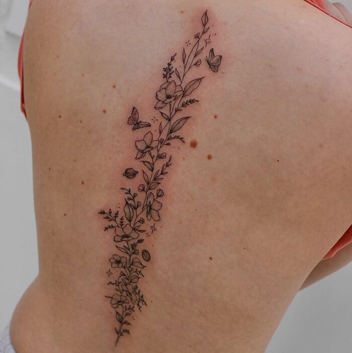 Delicate floral spine tattoo with butterflies emphasizing beauty and detail.