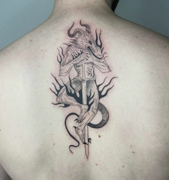 A beautifully detailed spine tattoo featuring a horned creature with flames on the back.