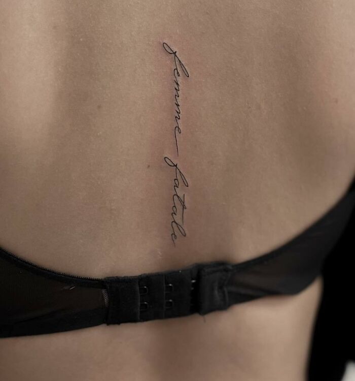Elegant spine tattoo in cursive reading "Femme Fatale," showcasing beautiful body art.