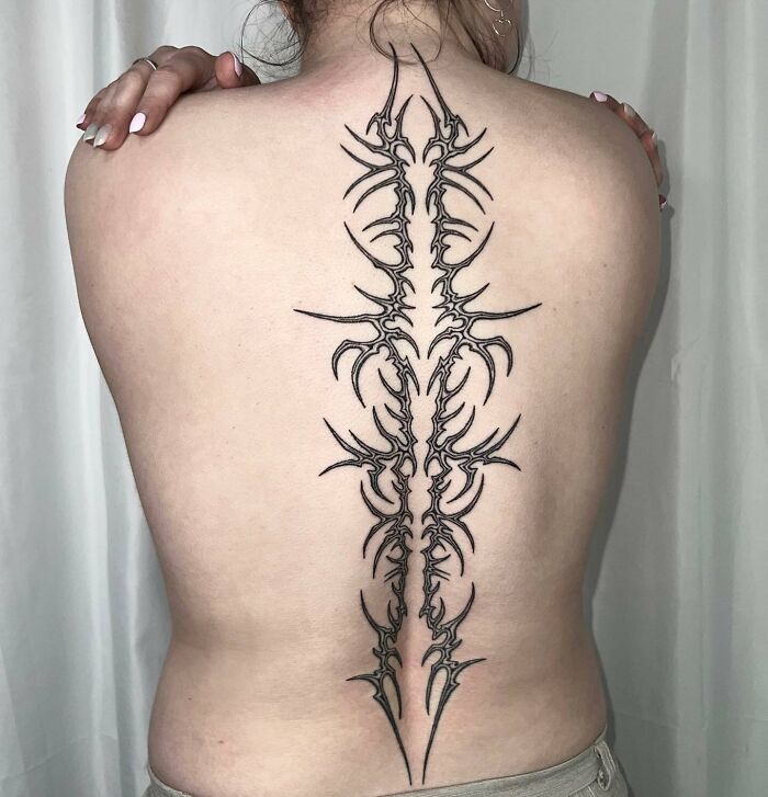 Elegant, intricate spine tattoo design on a person's back, showcasing bold symmetrical patterns.