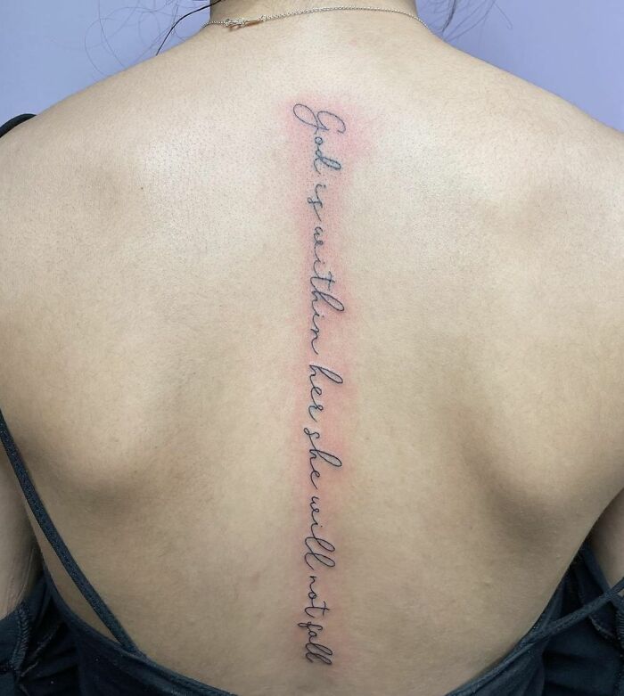 Spine tattoo with cursive quote on a woman's back, showcasing beautiful tattoo art.
