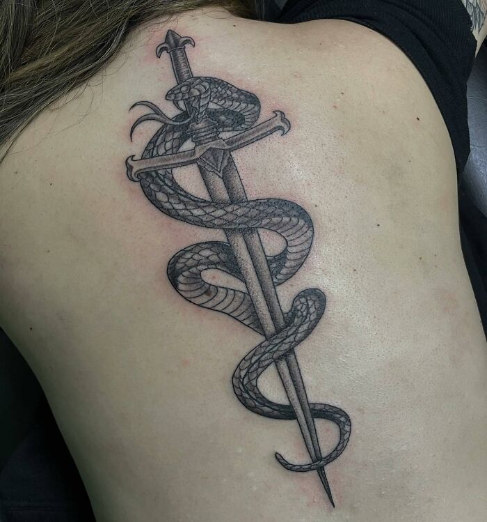 A detailed spine tattoo featuring a snake entwined around a sword, showcasing bold design elements.