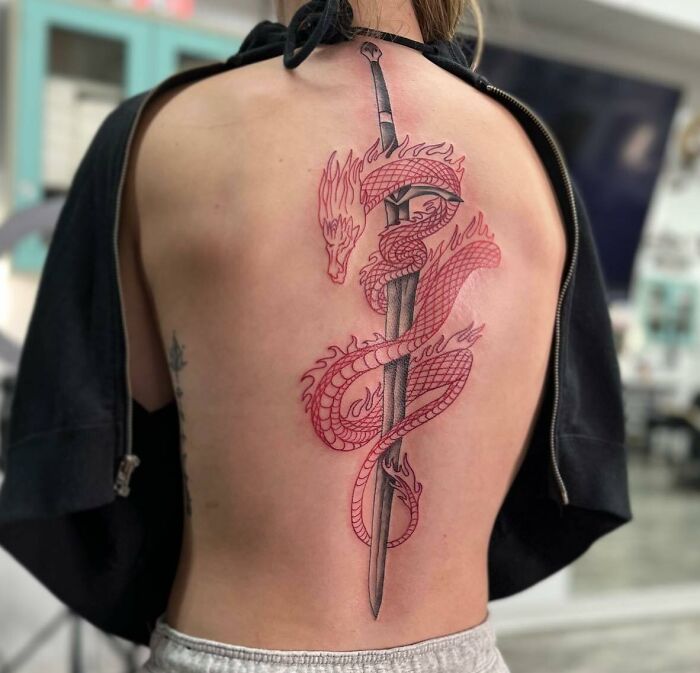 A detailed spine tattoo featuring a red dragon wrapped around a sword.