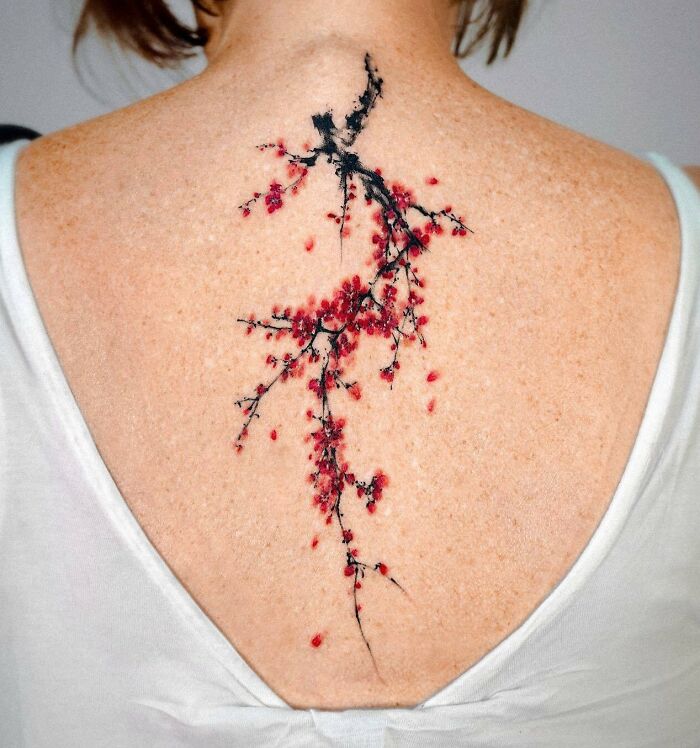 Spine tattoo with a delicate plum blossom design in black and red ink on a woman's back.