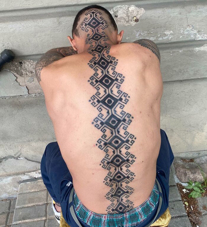 Geometric spine tattoo design running from neck to lower back on a seated person.
