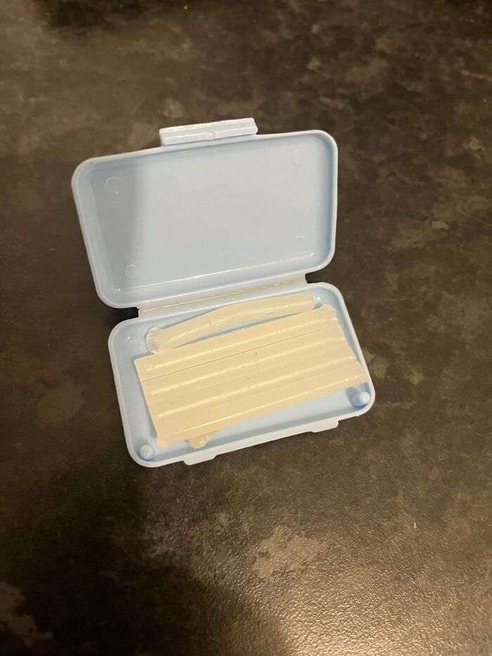 Small open blue plastic case containing unknown white ridged mysterious object on dark surface.