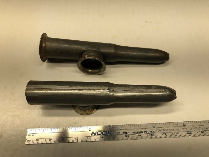 Two mysterious metal objects with flared ends placed next to a ruler for size reference on a light surface.