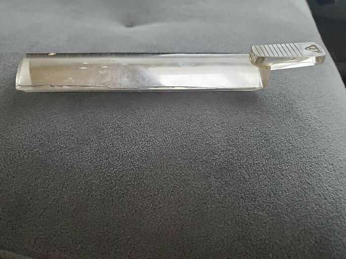 Clear rectangular mysterious object with a handle placed on a gray surface, prompting curiosity and intrigue.