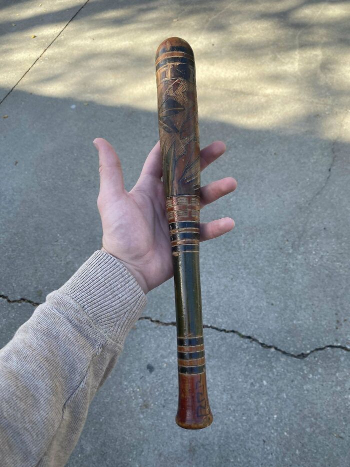 Hand holding a small vintage wooden object with painted and carved details, a mysterious object found outdoors.