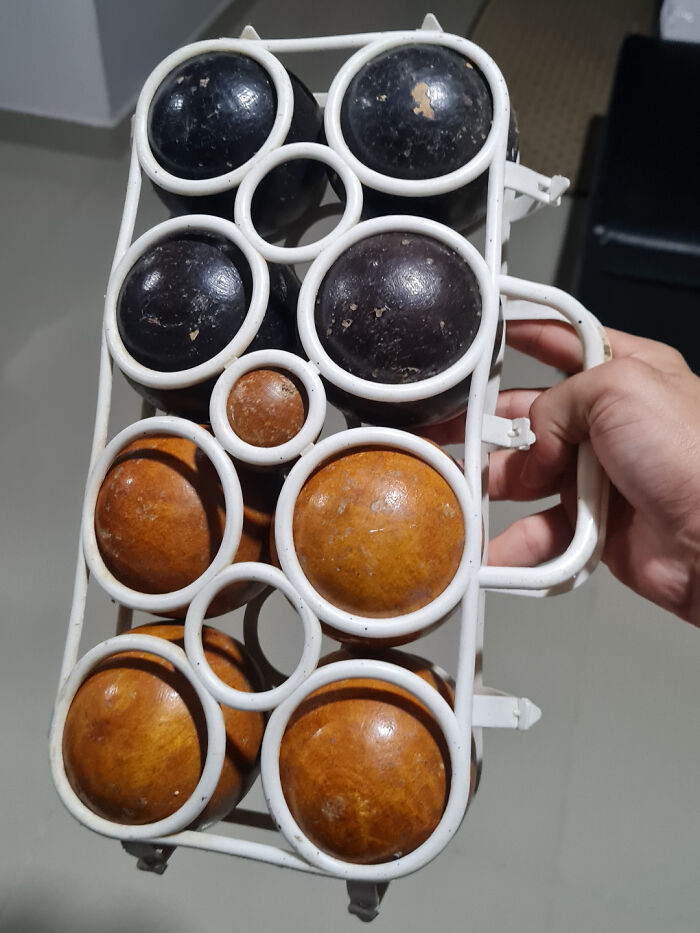 Hand holding a white metal rack containing mysterious black and brown wooden balls, an unusual object discovery.