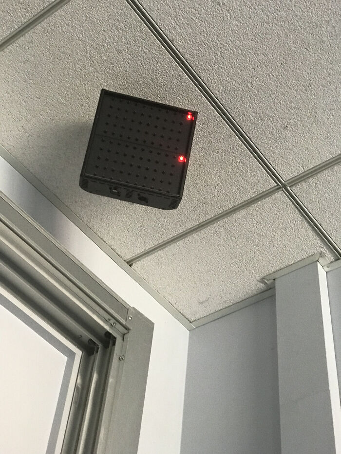 Black ceiling-mounted device with two red lights, possibly a mysterious object people stumbled upon indoors near a door frame.