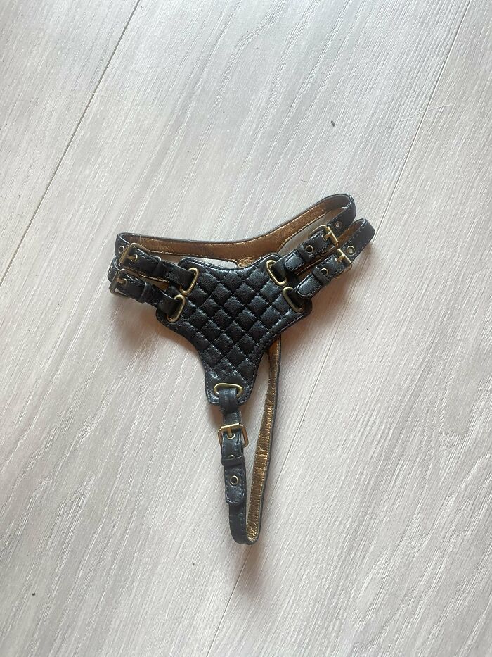 Black quilted leather object with buckles and straps laid on wooden floor, a mysterious object people stumbled upon.