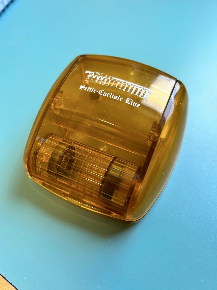 Post-It Note Sized, 1.5’’ Tall Orange Transparent Plastic Thing With A Hinged Lid That Opens Up And A Ridged Cylinder That Spins Inside. Marked With ‘Settle-Carlisle Line’. Found In An Old Office Space