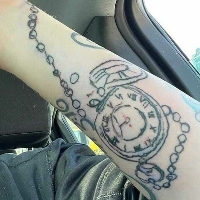 Failed tattoo of a pocket watch poorly drawn on an arm, featuring uneven lines and distorted clock face.
