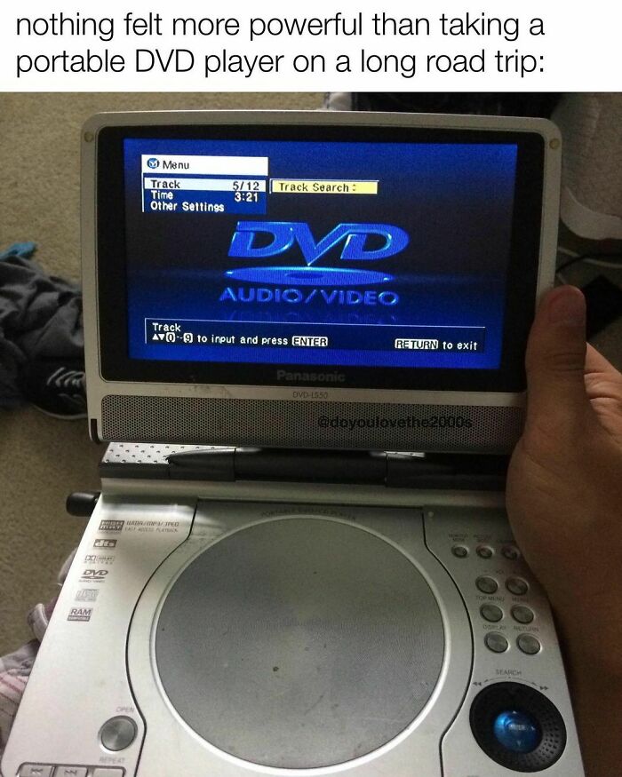 Portable DVD player from the 2000s showing a DVD menu screen, held by a person on a road trip.