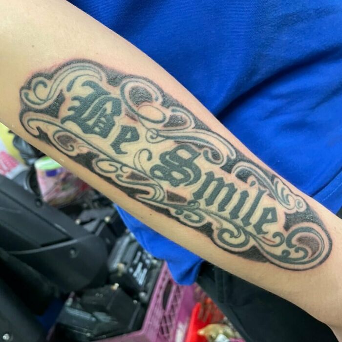 Failed tattoo on forearm with text "Be Smile" in decorative script.