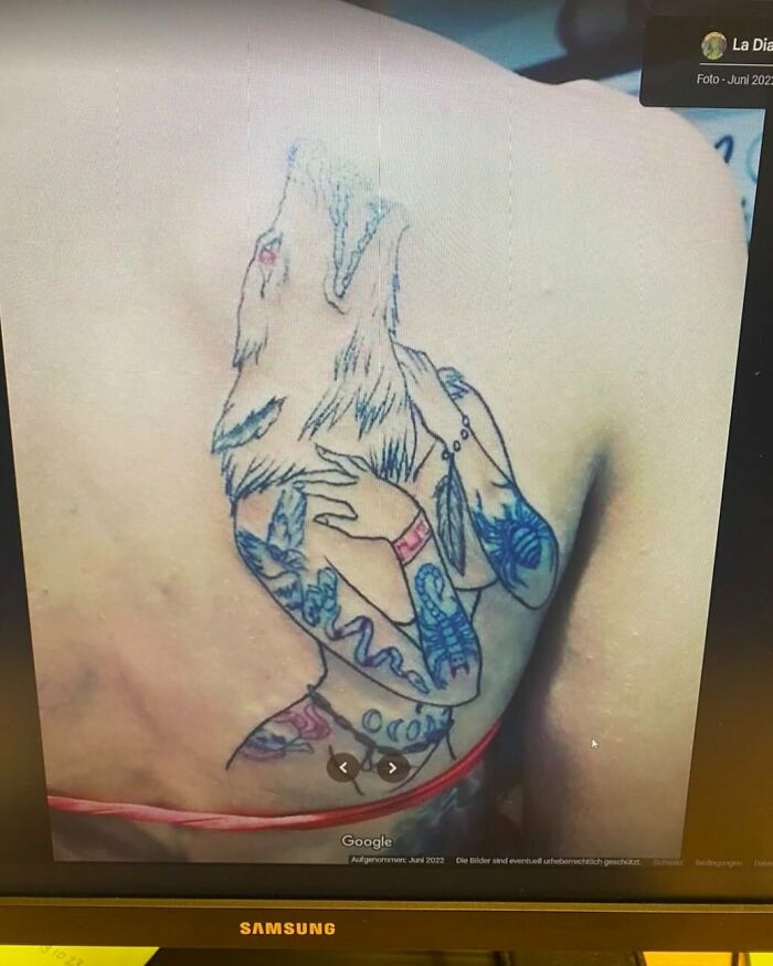 Failed tattoo with abstract wolf on shoulder blade, showcasing mismatched colors and design elements.