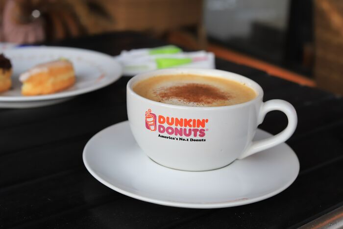 Close-up of a Dunkin Donuts coffee cup on a saucer with donuts blurred in the background, highlighting memorable strangers.