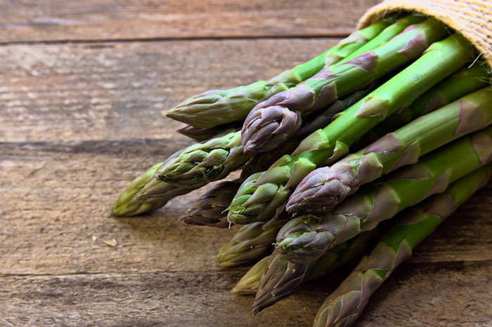 Bunch of fresh asparagus spears on a wooden table.