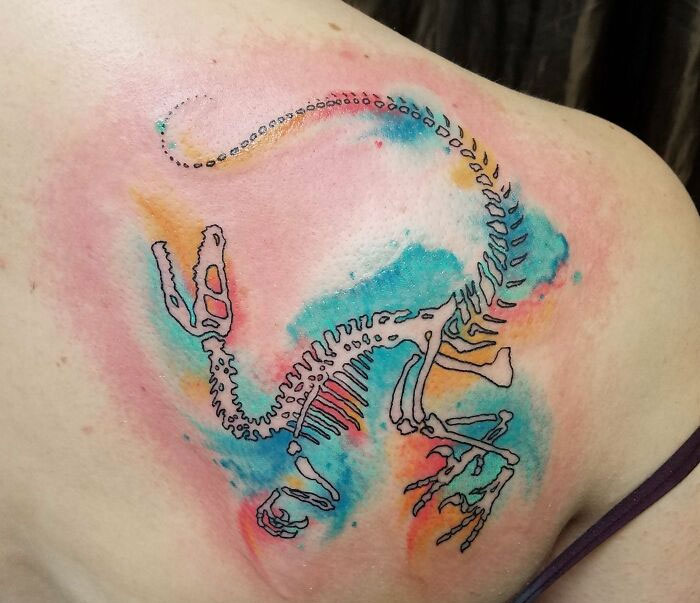 Watercolor dinosaur tattoo on shoulder, featuring vibrant hues and intricate skeletal design.